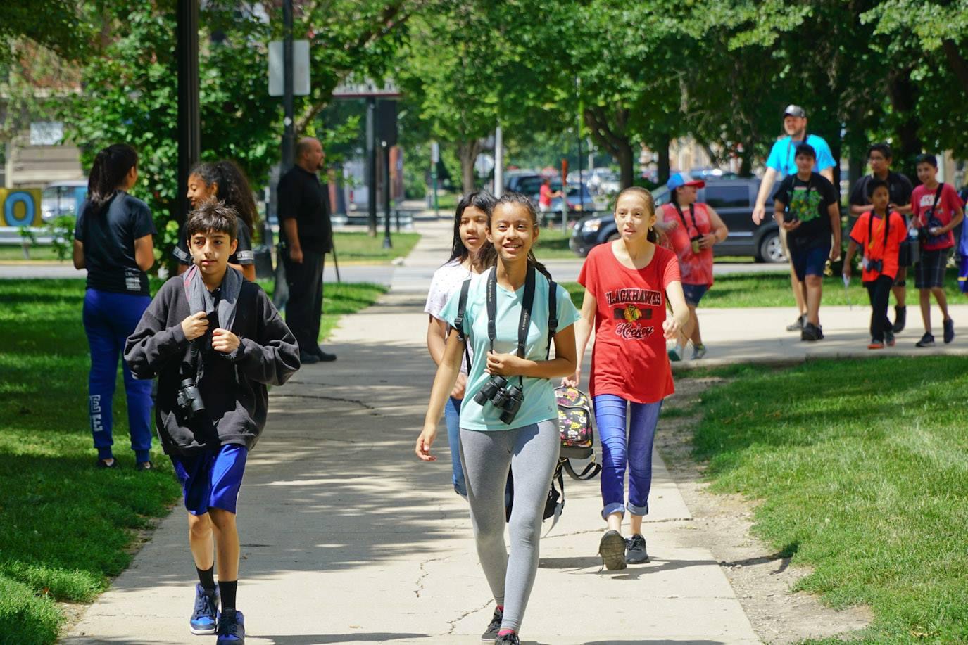 A group of teens walk towards the camera on an urban greenway